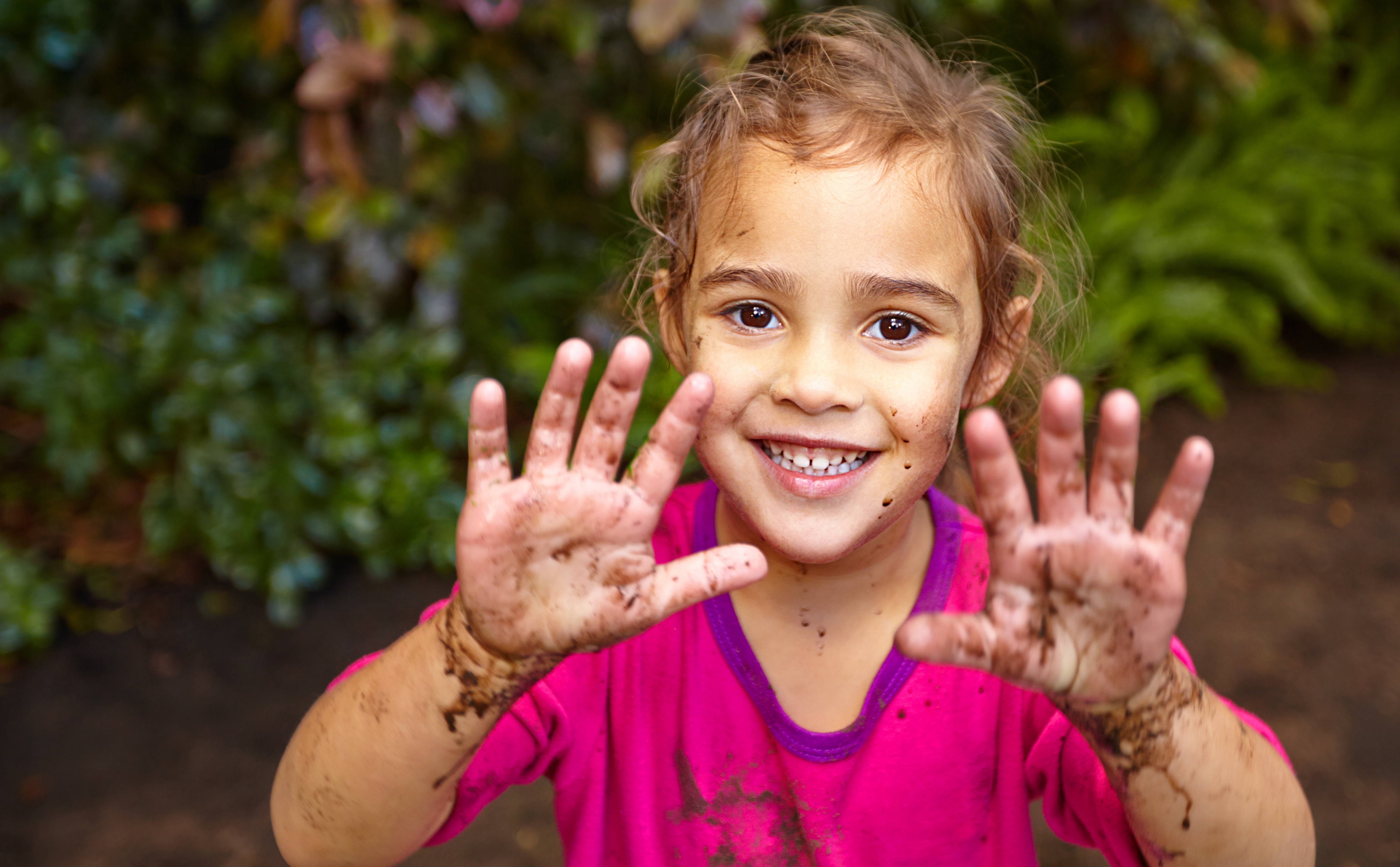 girl in pink holds up muddy hands
